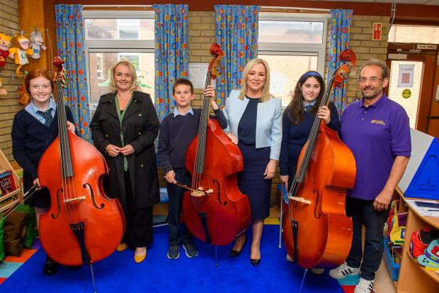 First Minister Michelle O’Neill (centre) and Junior Minister Pam Cameron (second from left) pictured with P7 pupils from Good Shepherd PS who were having a double bass lesson, led by Crescendo tutor Ricky Matson (right).
